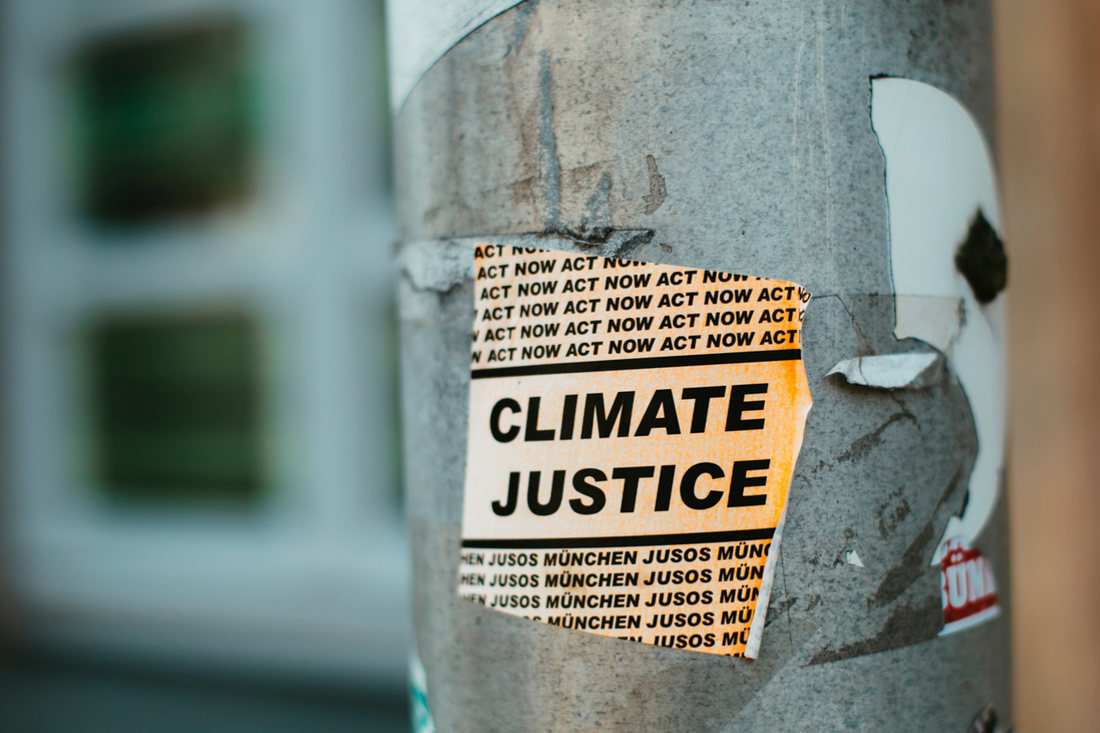 Picture of a sticker on a street pole saying Climate Justice. Act now.