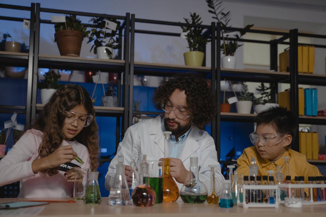 Picture of a teacher and students in front of chemistry vials and beakers.